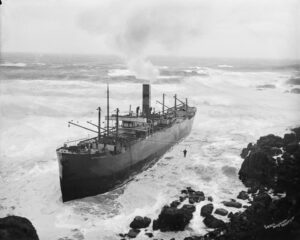 G14049; City of Cardiff (1906). Port just off bow view. Man in breeches buoy about half way to cliffs. Rough seas. Taken from cliffs.